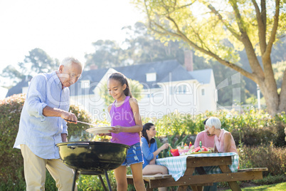 Grandfather and granddaughter preparing barbecue for their family