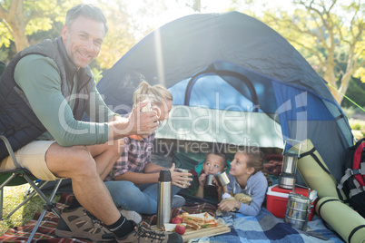 Family having snacks and coffee outside the tent at campsite