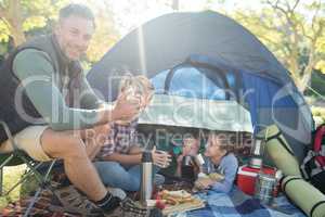 Family having snacks and coffee outside the tent at campsite