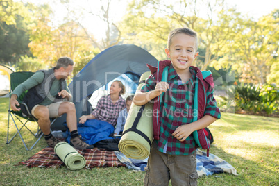Boy holding a rolled mat while family sitting in the tent