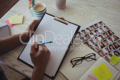 Hands of photo editor writing on clipboard at creative office desk