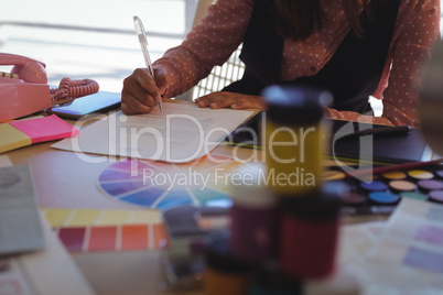 Mid section of businesswoman writing on paper at office desk