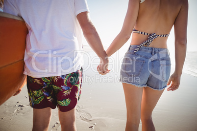 Mid section of couple holding hands at beach