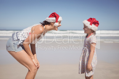 Cheerful woman with daughter wearing Santa hat at beach