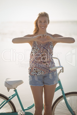 Portrait of woman making heart shape with hands standing at beach
