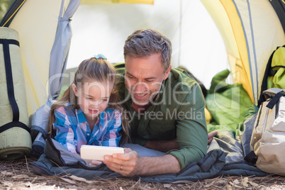 Father and daughter using mobile phone at campsite