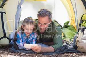 Father and daughter using mobile phone at campsite