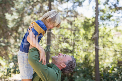 Playful father lifting up son in forest