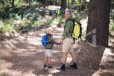 Smiling father and son carrying backpack while hiking in forest