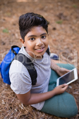 High angle portrait of boy sitting with tablet PC in forest
