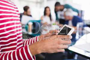 Midsection of businesswoman using phone while sitting with colleagues