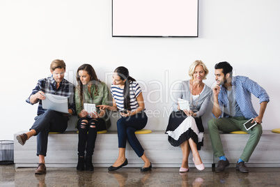 Business people using technologies while sitting against wall