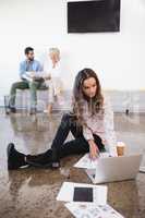 Businesswoman using laptop on floor at creative office