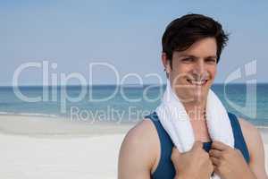 Smiling man standing on beach with towel around his neck