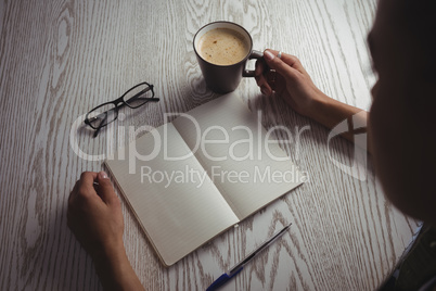 Businesswoman holding coffee cup on desk in office