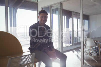 Smiling businessman sitting on table in modern office