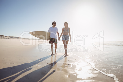 Young couple holding hands at beach during sunny day
