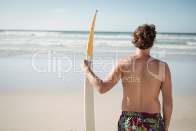 Rear view of shirtless man holding surfboard at beach