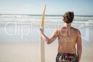 Rear view of shirtless man holding surfboard at beach