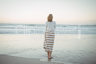 Rear view of woman standing at beach during dusk