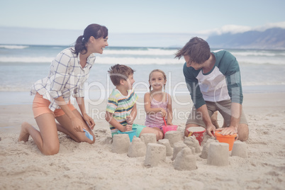 Happy siblings with parents making sand castle