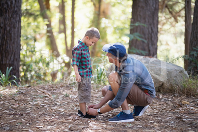 Father tying shoelace of son in forest