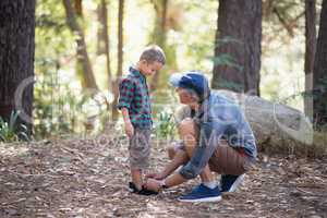 Father tying shoelace of son in forest