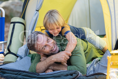 Playful little boy lying on father in tent