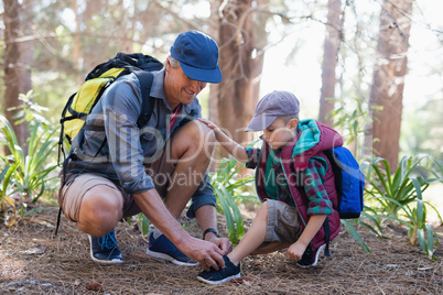 Father tying shoelace for son in forest