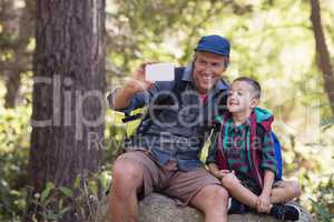 Happy father sitting with boy on rock taking selfie
