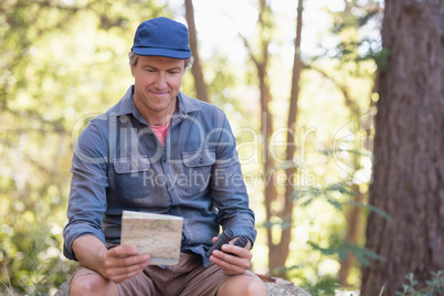 Happy hiker reading map while sitting on rock