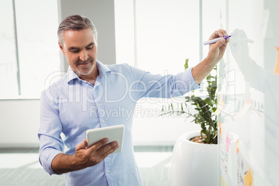 Attentive executive using digital tablet while writing on whiteboard