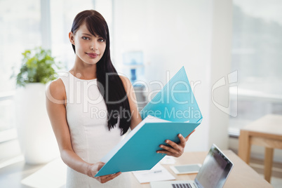 Portrait of beautiful executive holding file at desk