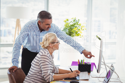 Graphic designers discussing over personal computer at desk