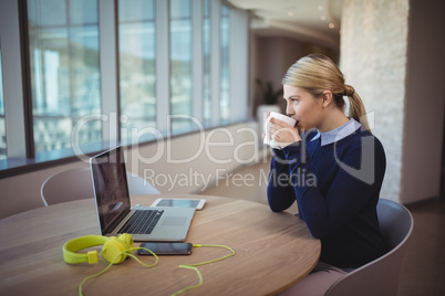 Female executive having cup of coffee at desk