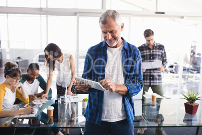 Happy businessman using digital tablet with team working in background