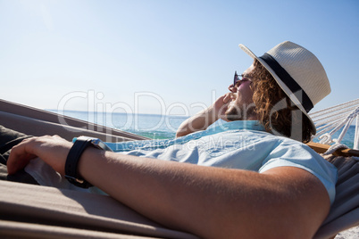 Man relaxing on hammock and talking on mobile phone on the beach