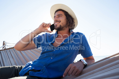 Man relaxing on hammock and talking on mobile phone on the beach