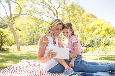 Happy mother and daughter using digital tablet in park