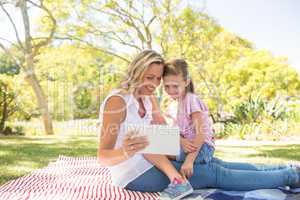 Happy mother and daughter using digital tablet in park