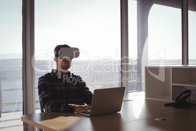 Businessman using virtual reality headset and laptop in office