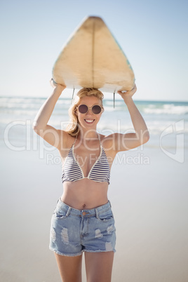 Portrait of young woman carrying surfboard at beach