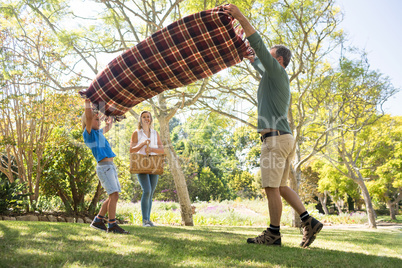 Father and son spreading the picnic blanket while mother carrying basket