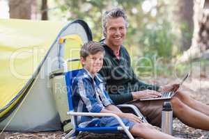 Smiling father and son with laptop in forest
