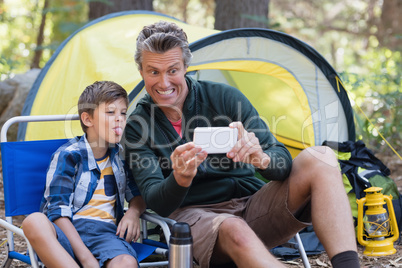 Father and son taking picture by tent in forest