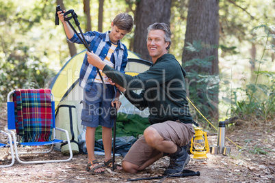 Smiling father giving hiking pole to son in forest