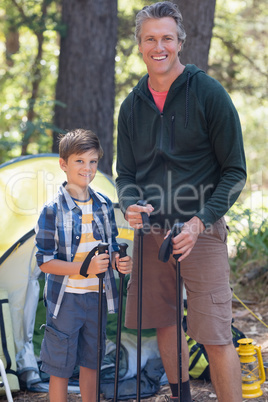 Smiling father and son holding hiking poles in forest