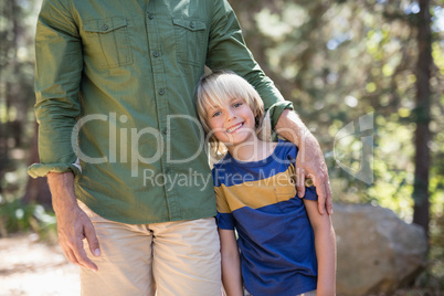 Smiling boy standing with father on sunny day in forest