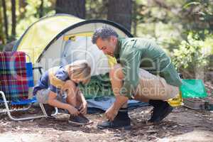 Father and son tying shoelace by tent at campsite