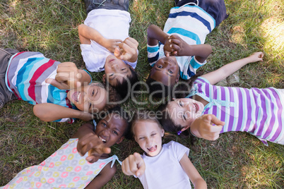 Portrait of smiling friends pointing up while lying on grassy field